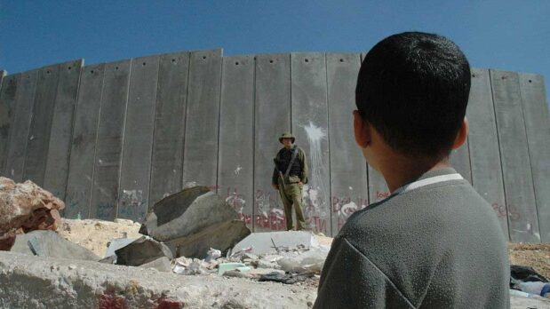 A Palestinian boy and an Israeli soldier by Israel's illegal separation wall in the West Bank. (Justin McIntosh/CC BY 2.0)