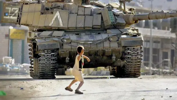 A screenshot from the film Occupation of the American Mind showing a Palestinian boy throwing a rock at an Israeli tank.
