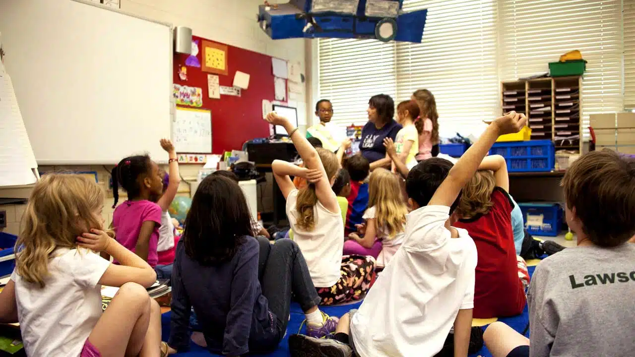 Children seated on a classroom floor listening to their teacher read an illustrated storybook (Photo by CDC, licensed under Unsplash License)